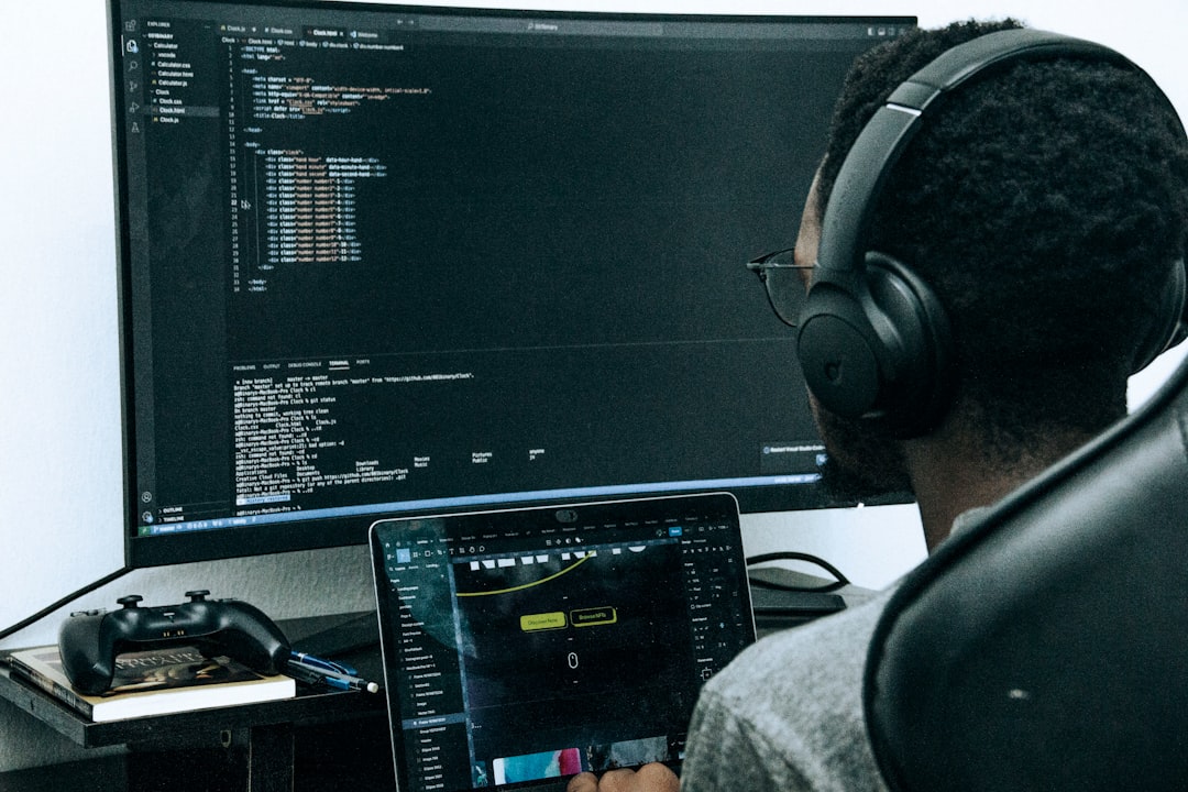 A focused developer working on code, using dual screens. The primary monitor displays a coding editor, while the laptop shows a UI design tool. Wearing headphones, the developer works in a quiet, minimal workspace, emphasizing productivity and tech innovation. Ideal for themes like coding, programming, web development, and tech workspace inspiration.